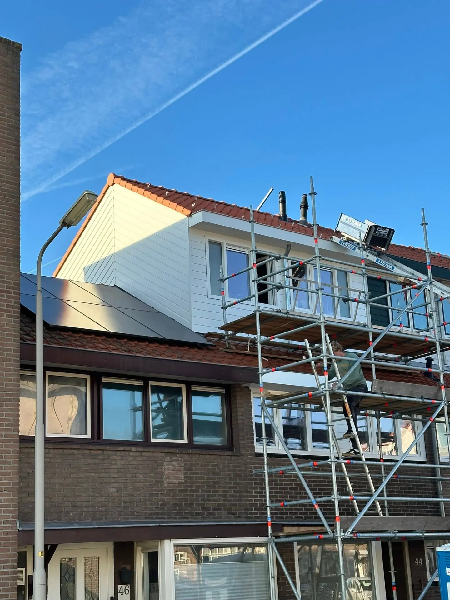 Nieuwe opbouw met witte betimmering op een woning, met steiger ervoor